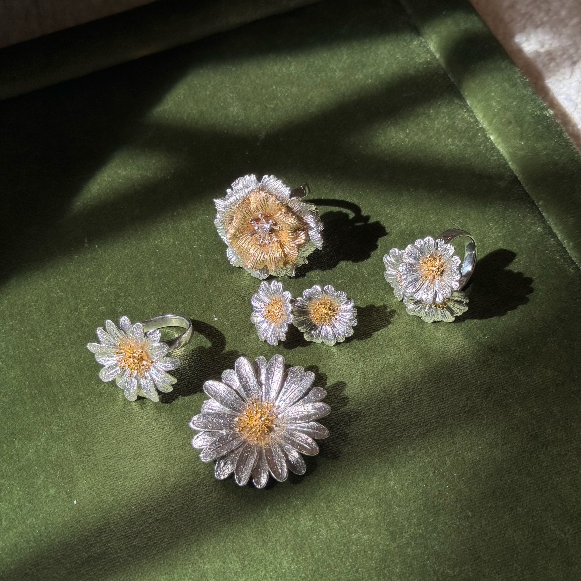 Italian silver floral jewelry collection featuring textured silver petals and gold-tone flower centers, displayed on rich green velvet.